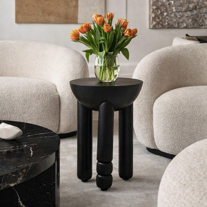 Black side table with a vase of orange tulips in a living room setting.